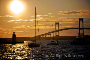 Photographed near the Connecticut Turnpike, when the big, round, radiant, yellow Sun, green beaming light from the lighthouse, tall masks of sailboats, the shining clouds and water are one golden sunset.