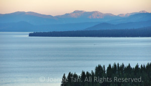Photographed at the North Shore of Lake Tahoe, California after a summer sunset, a painting-like lake and mountain view of purple mountains, blue water, green trees and warm rays on snow capped top.