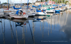 Boats docked in the peaceful harbor of Brittany, France, reflections of blue sky, clouds, and shimmering masks in water. Photographed in the port city of paimpol.