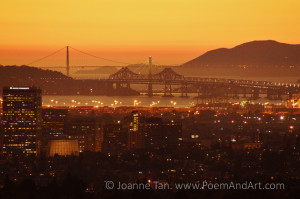 A nighttime landscape of the Pacific Ocean, orange sky, shimmering lights, Golden Gate Bridge, & the new and old Bay Bridges, photographed at dusk from a hill behind Oakland, CA.