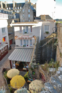 Stone staircase leading from the city wall down to a restaurant below inside of the city of St. Malo, with yellow umbrellas over open air outdoor diners.