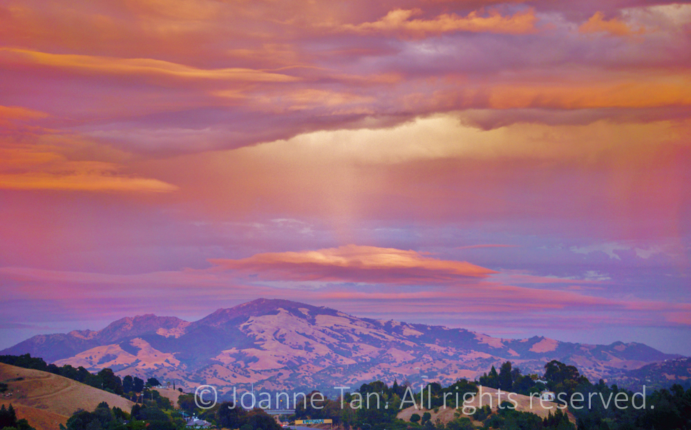 Heavenly light casting down through beautiful orange, purple, red and yellow colored sunset clouds, over another cloud above Mt. Diablo, California. Photographed on a glorious September dusk.
