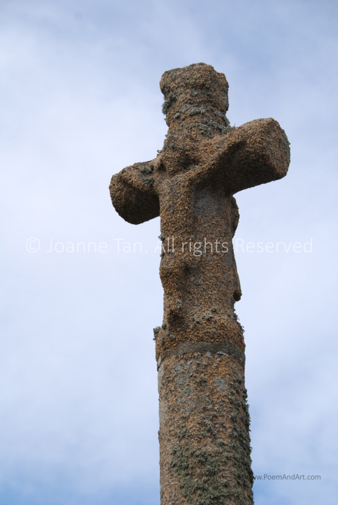A sculpture of a stone cross worn out by elements of rain, Sun, and wind, with a crucified Savior's image almost faded. Picture taken in Paimpol, Brittany, France.