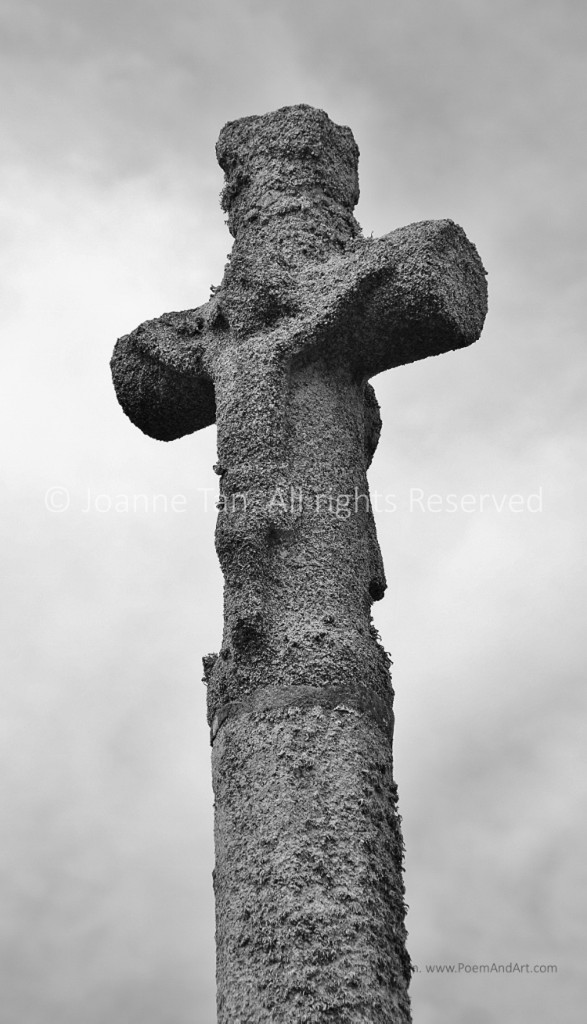 An ancient stone cross with Jesus Christ crucifixion image weathered and barely visible. Black & white photo. Brittany, France.
