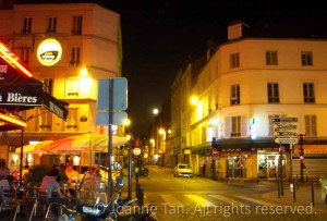 Street lights and a full Parisian/Parisien Moon aglowing the buildings with yellow, orange colors, a Restaurant diners sitting outside on the street corner, on a hot summer night. Paris, France.
